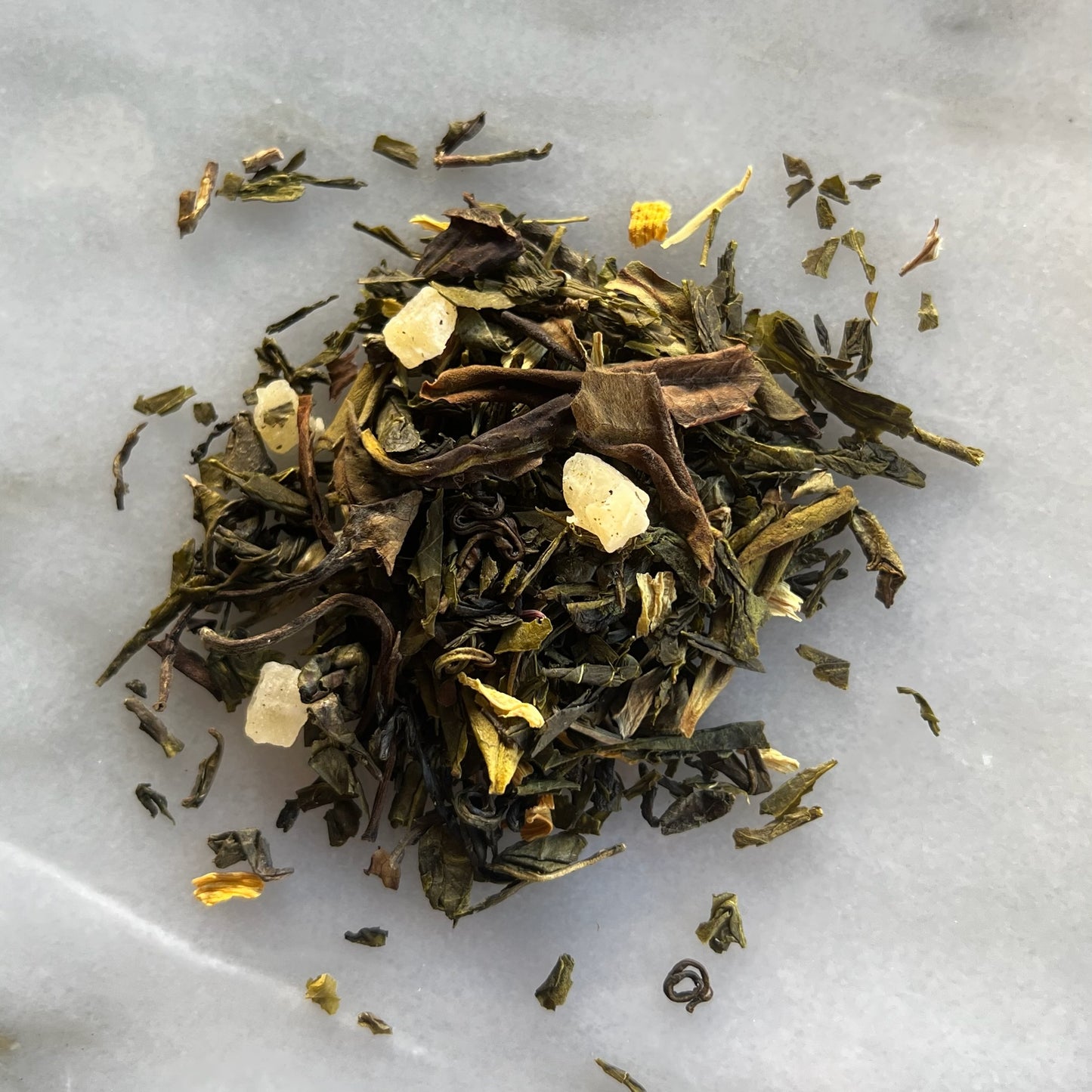 En hög med grönt löste "Alice blanding" på en marmorbricka som visar teets färg och struktur.