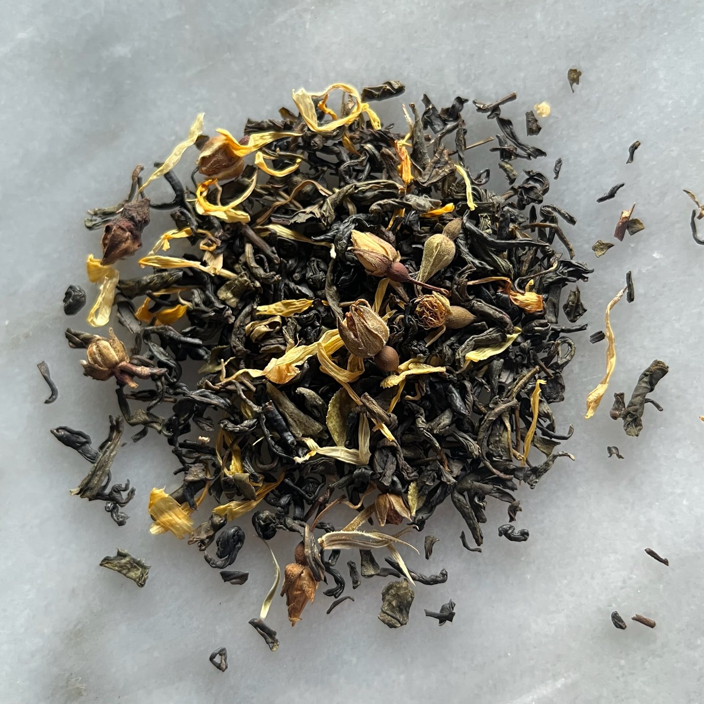 En liten tehög med teet Blå Passion, liggandes på en vit marmorbricka där man kan se teets färg och struktur