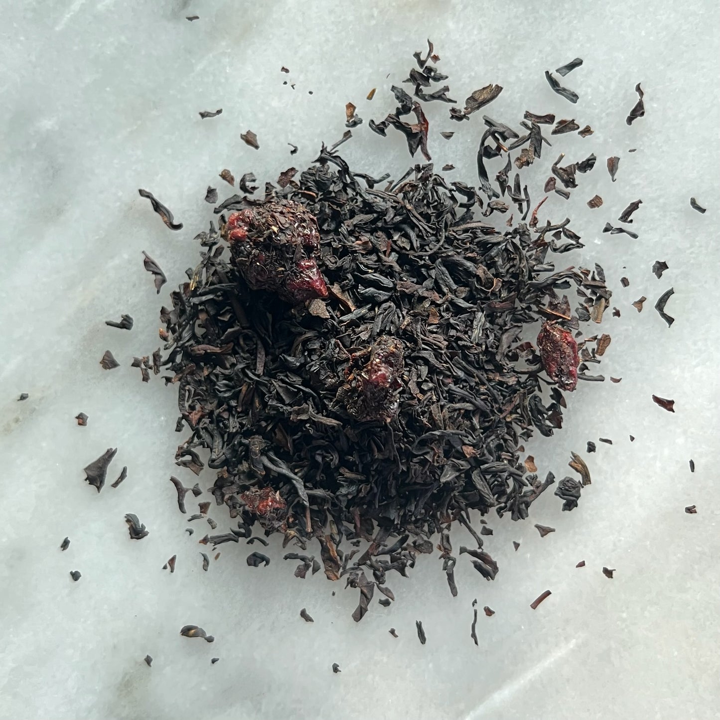 Löst svart körsbärs-te på en marmorbricka som visar teets färg och struktur.