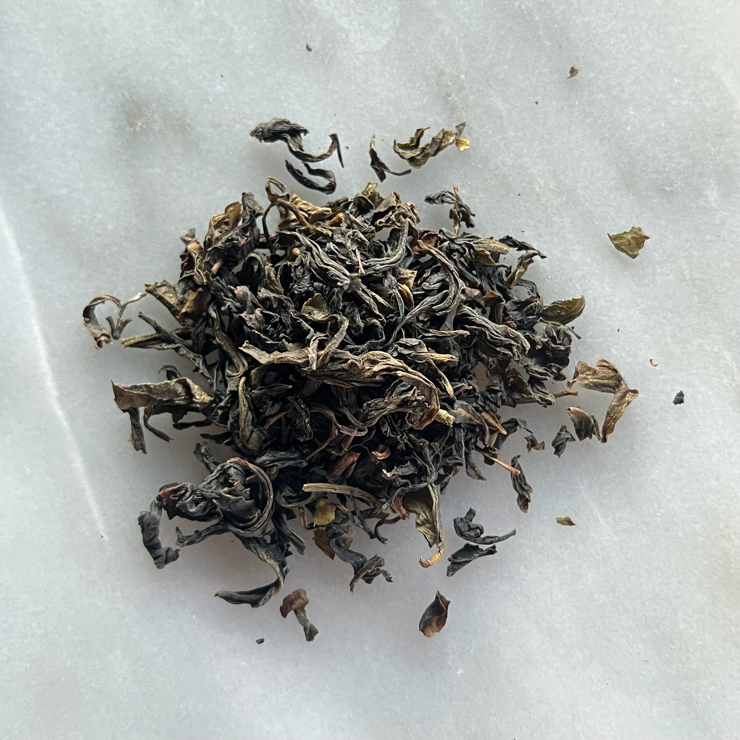 En liten tehög med teet formosa oolong, liggandes på en vit marmorbricka där man kan se teets färg och struktur