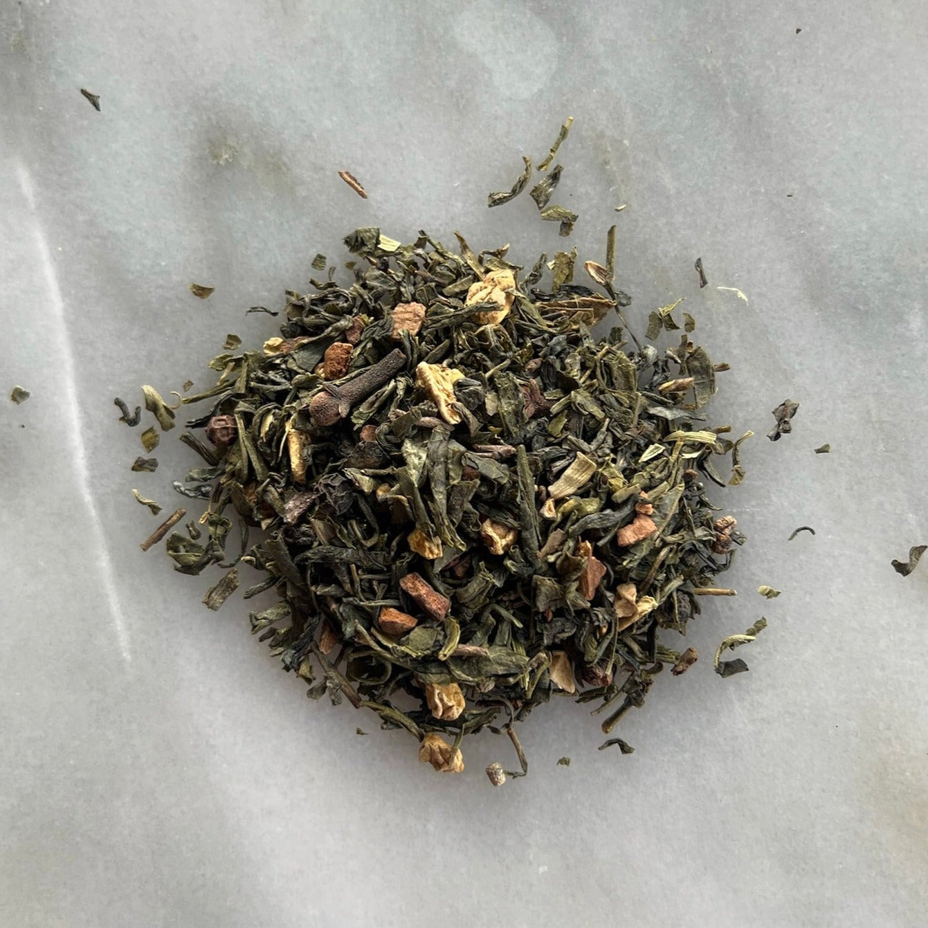 En liten tehög med teet Grön Chai, liggandes på en vit marmorbricka där man kan se teets färg och struktur
