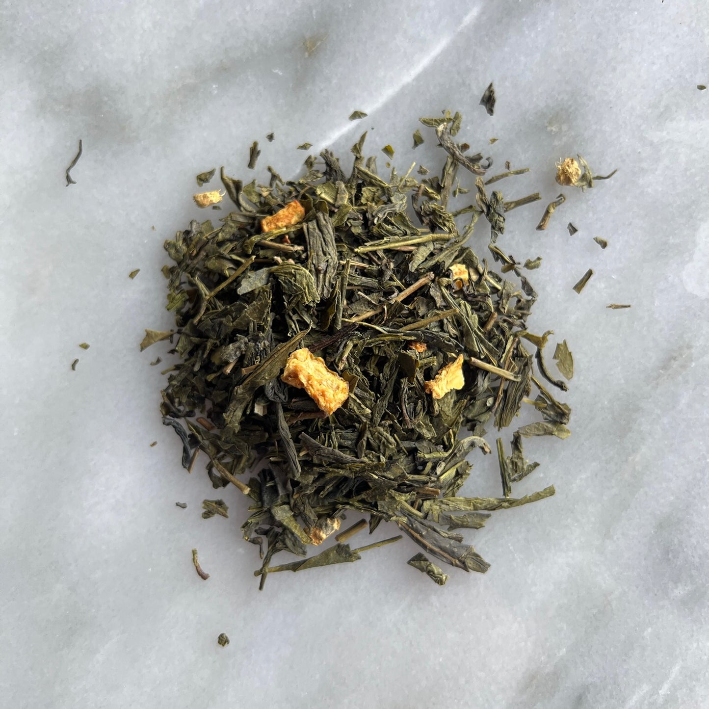 En liten tehög med teet Grön Frisk & Het, liggandes på en vit marmorbricka där man kan se teets färg och struktur