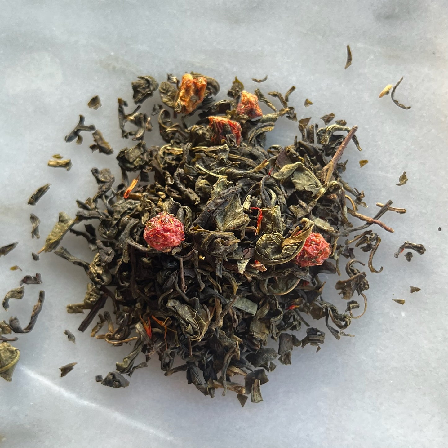 En liten tehög med teet Gröna löv & Röda Bär, liggandes på en vit marmorbricka där man kan se teets färg och struktur