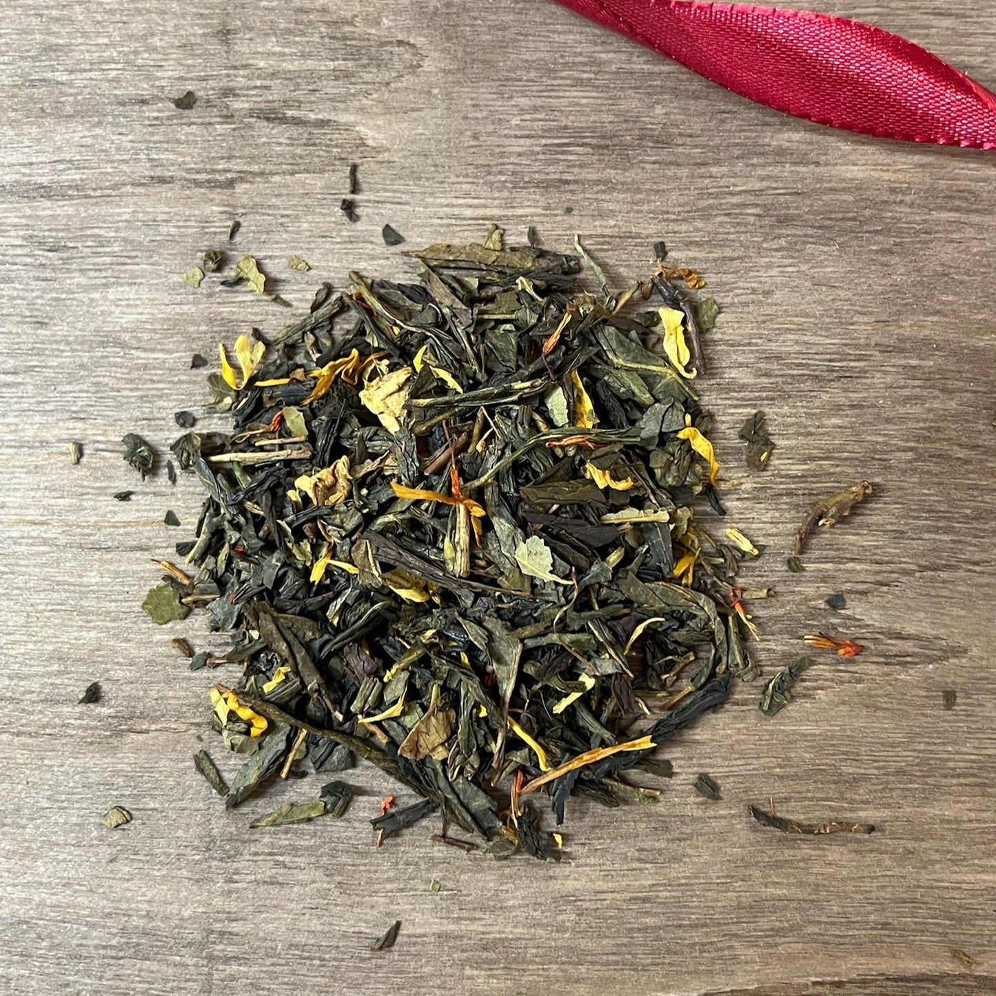 Grönt Höstmys på en träbricka där man ser teets struktur och innehåll, med ett rött sammetsband i bakgrunden.