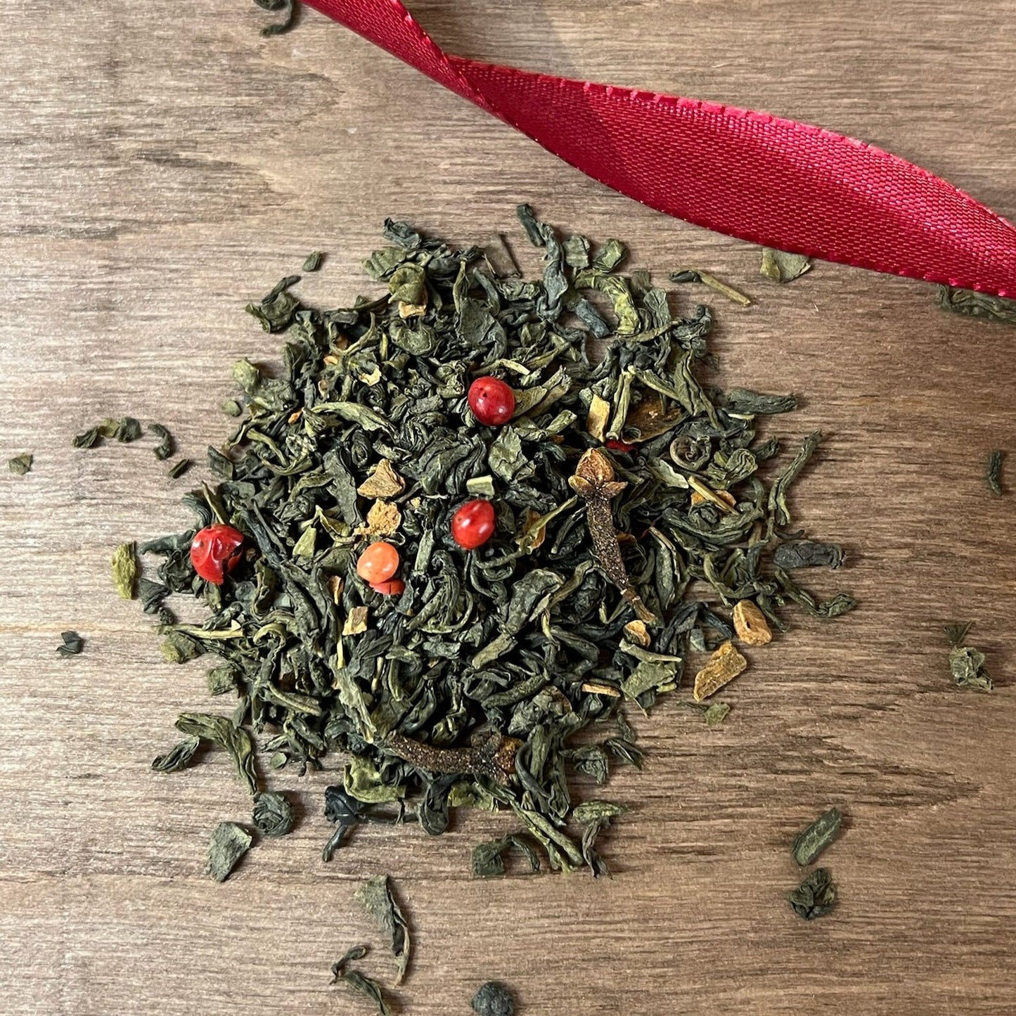 Grönt julte på en träbricka där man ser teets struktur och innehåll, med ett rött sammetsband i bakgrunden.