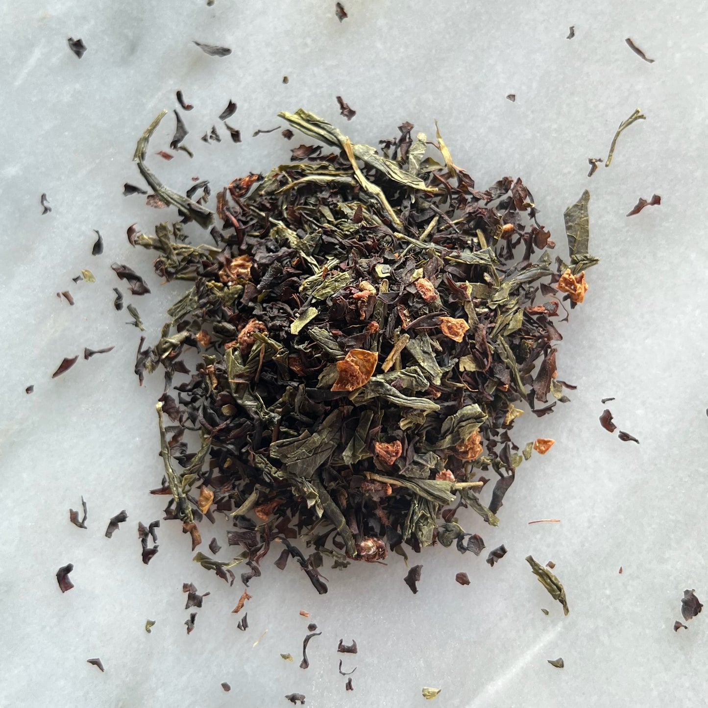 En liten tehög med det ekologiska gröna teet Hallon & Havtorn, liggandes på en vit marmorbricka där man kan se teets färg och struktur