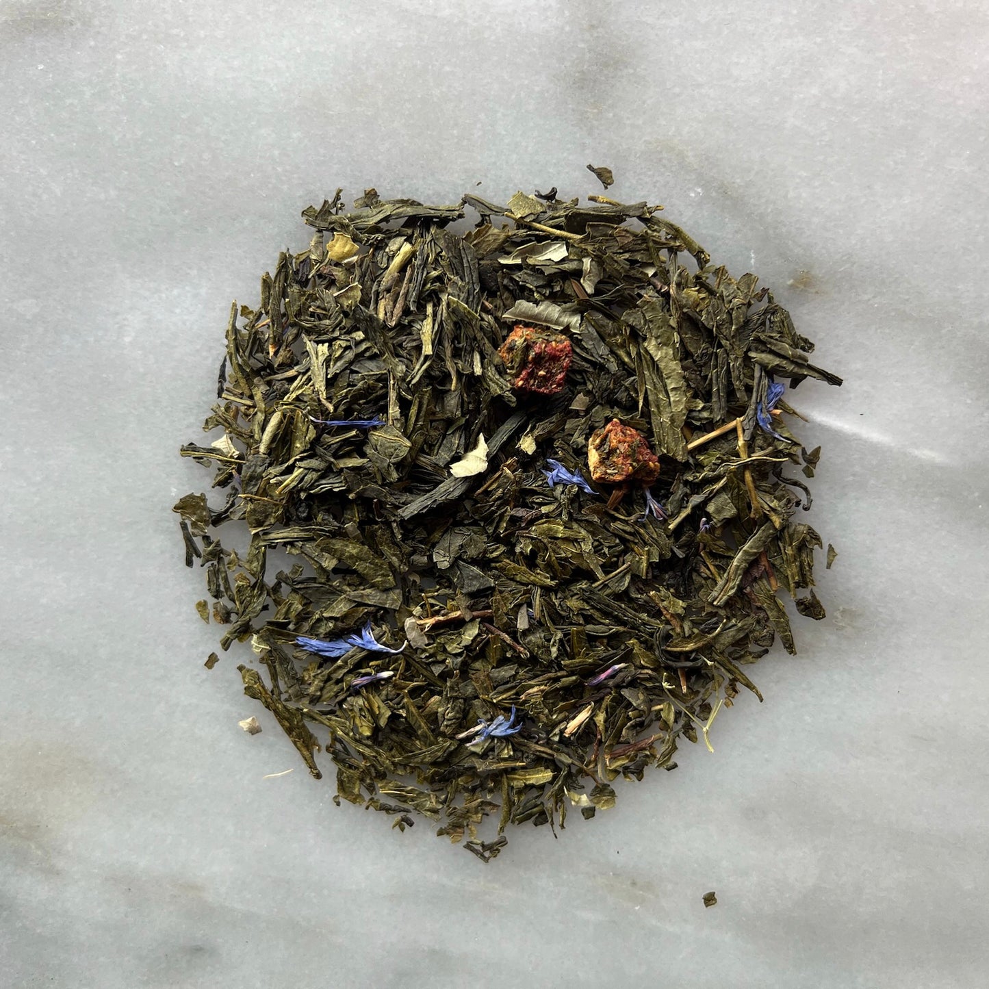 En liten tehög med det gröna teet Jordgubb & Champagne, liggandes på en vit marmorbricka där man kan se teets färg och struktur