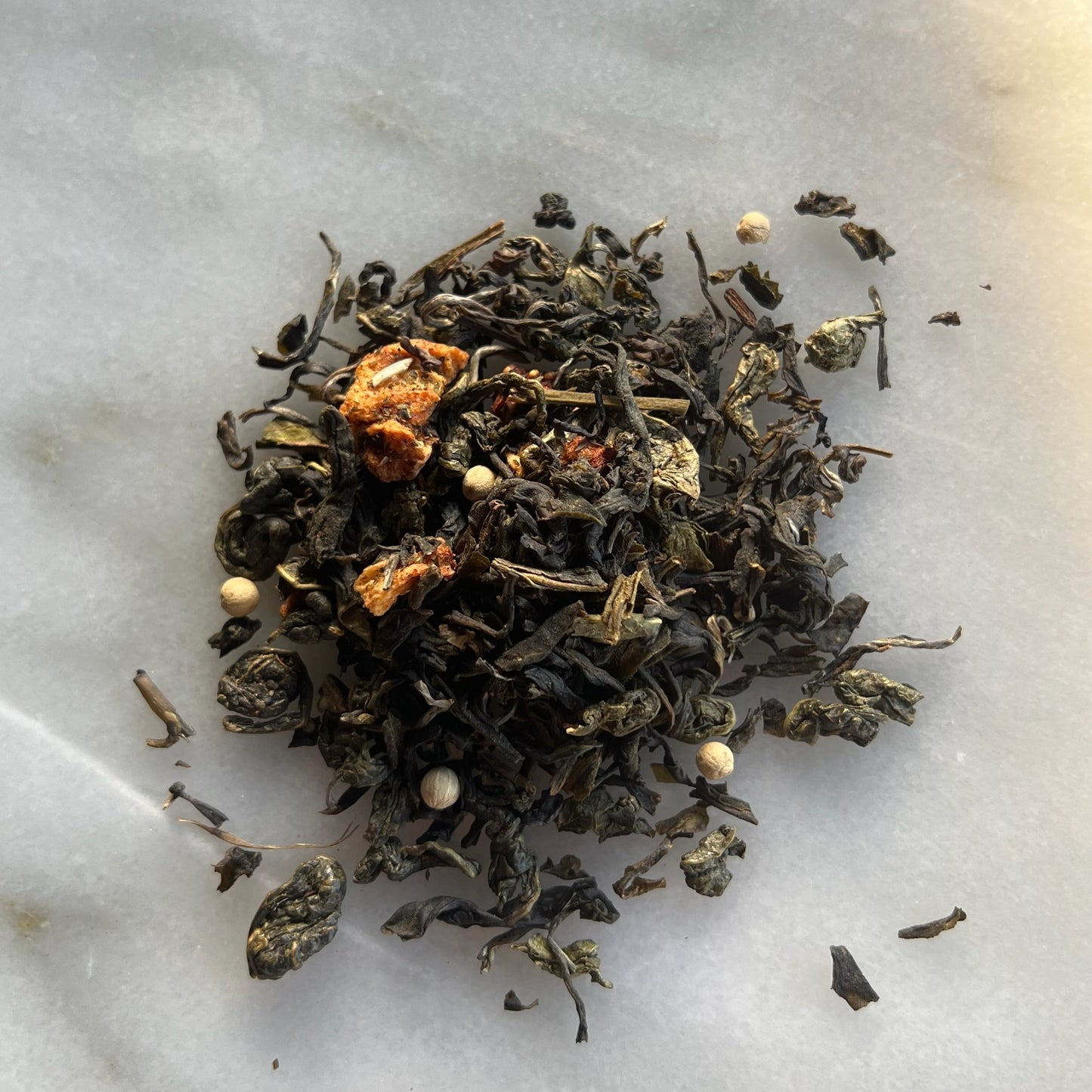 En liten tehög med det gröna teet Kiss Me Kate, liggandes på en vit marmorbricka där man kan se teets färg och struktur