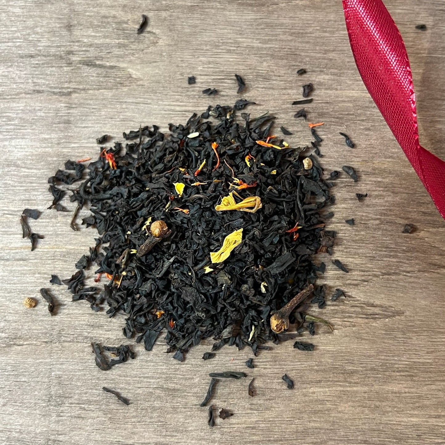 Svart julte Lusse Lelle på en träbricka där man ser teets struktur och innehåll, med ett rött sammetsband i bakgrunden.