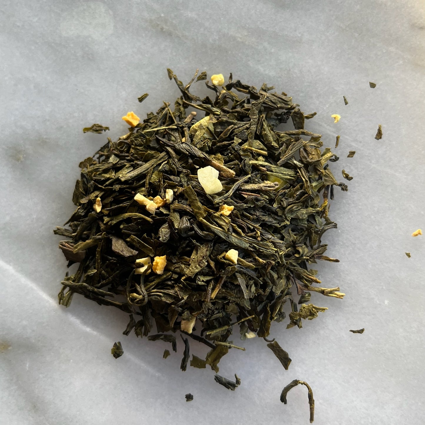 En liten tehög med det gröna teet Mangosorbet, liggandes på en vit marmorbricka där man kan se teets färg och struktur