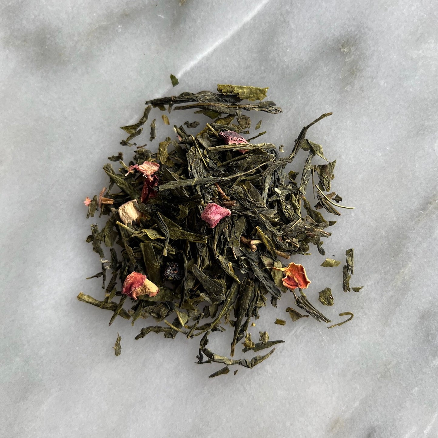 En liten tehög med det gröna teet Mosebacke, liggandes på en vit marmorbricka där man kan se teets färg och struktur