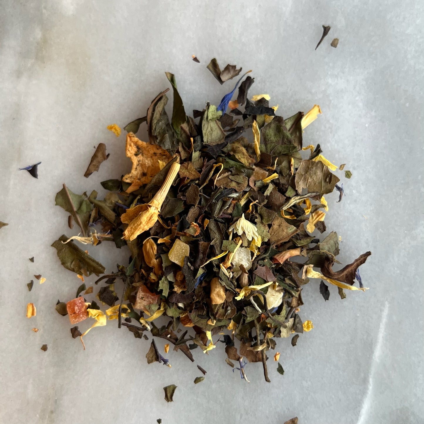 En liten tehög med det vita teet Mullbär, liggandes på en vit marmorbricka där man kan se teets färg och struktur