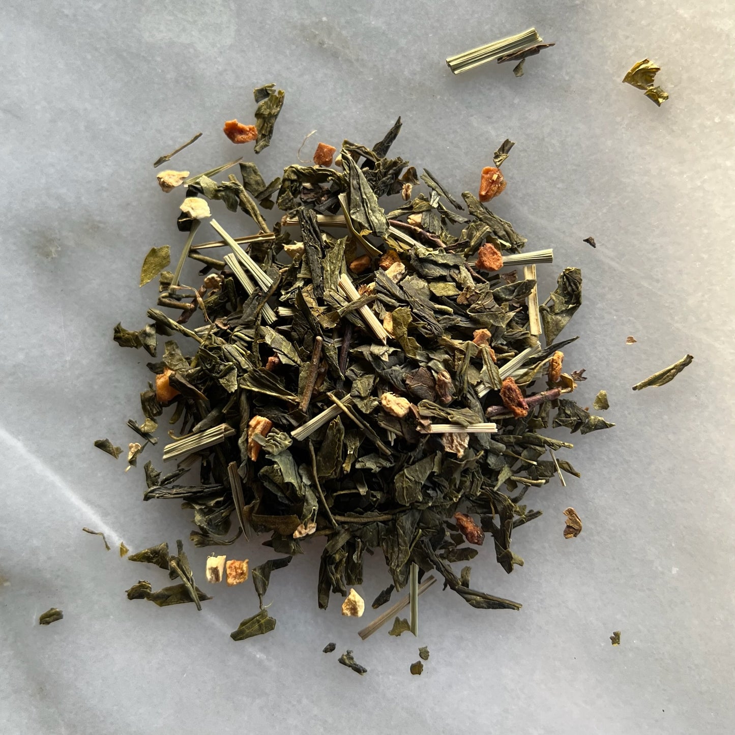 En liten tehög med det gröna teet Päron Ingefära, liggandes på en vit marmorbricka där man kan se teets färg och struktur