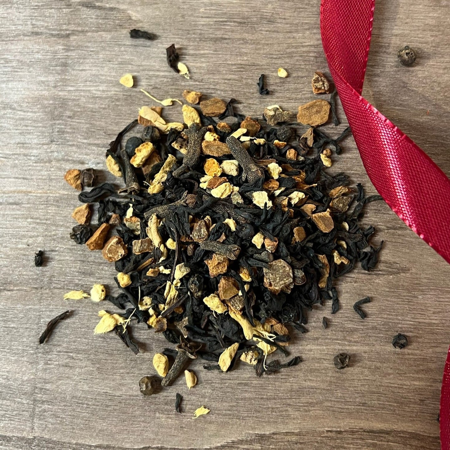 Svart julte Pepparkaka på en träbricka där man ser teets struktur och innehåll, med ett rött sammetsband i bakgrunden.