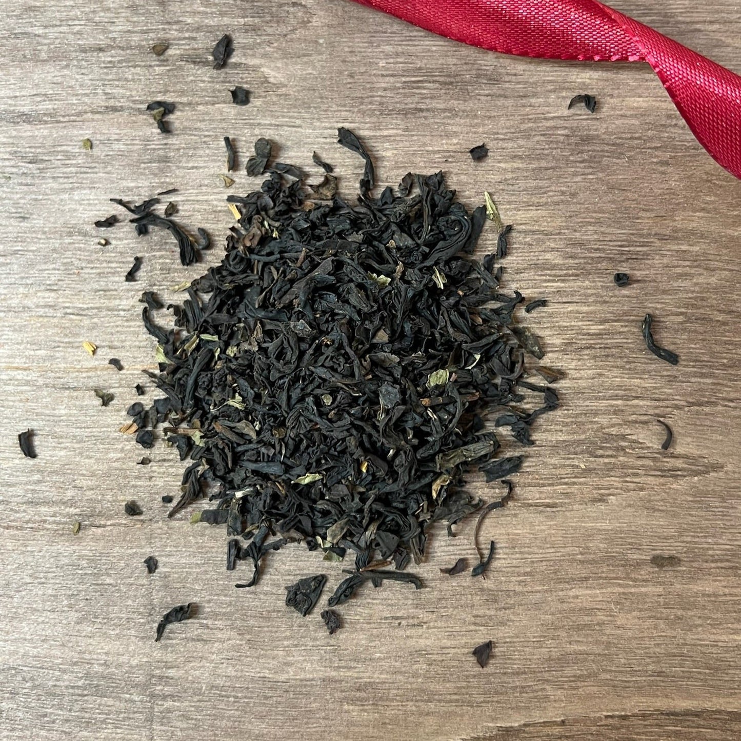 Svart julte "Polkagris" på en träbricka där man ser teets struktur och innehåll, med ett rött sammetsband i bakgrunden,