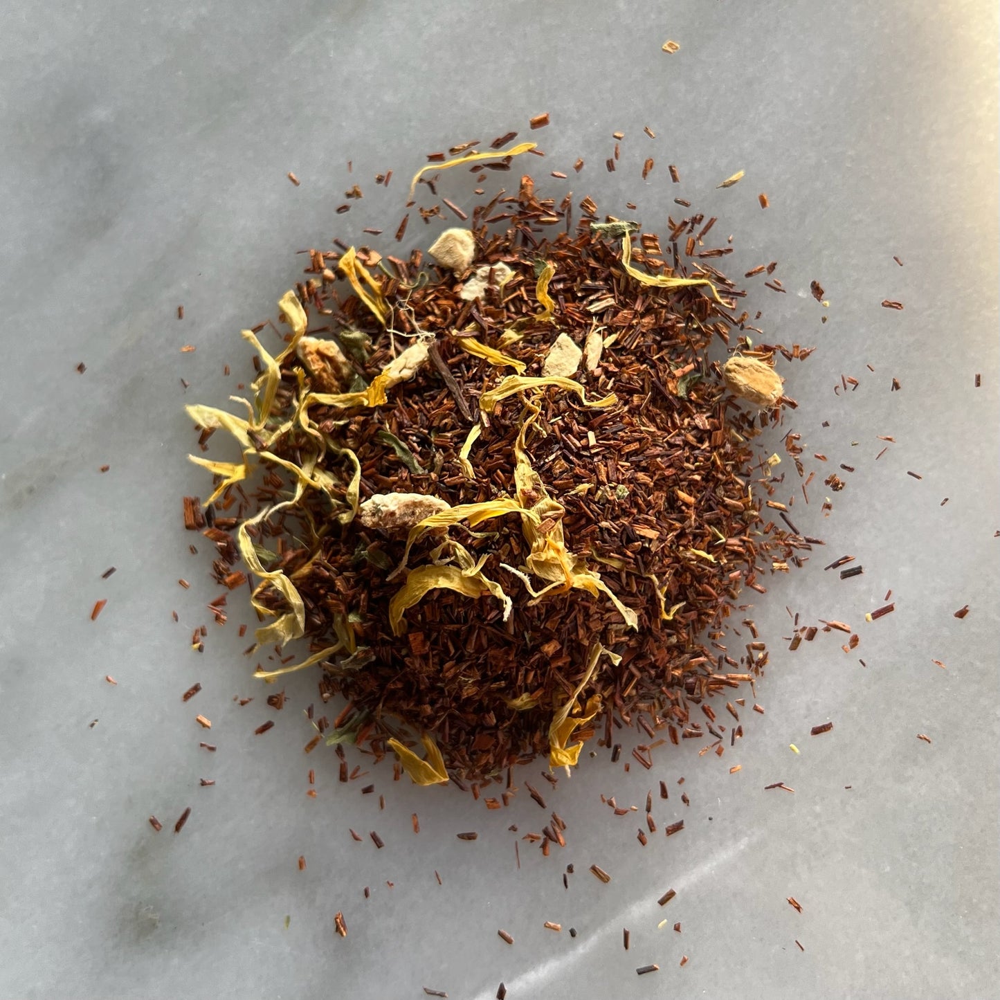 En liten tehög med det ekologiska röda teet Rooibos Grape Ingefärra, liggandes på en vit marmorbricka där man kan se teets färg och struktur