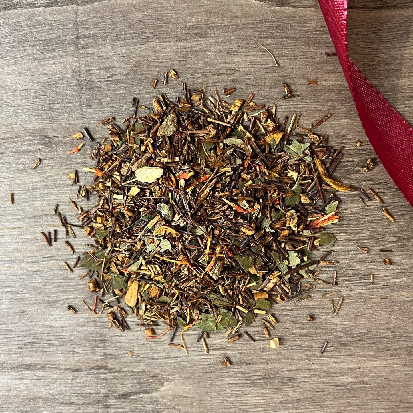 Rooibos julte på en träbricka där man ser teets struktur och innehåll, med ett rött sammetsband i bakgrunden.