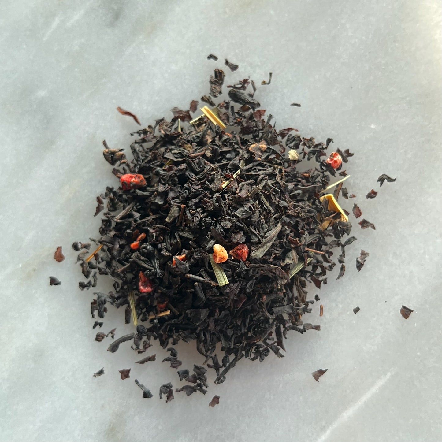 En liten tehög med det svarta teet Semester, liggandes på en vit marmorbricka där man kan se teets färg och struktur