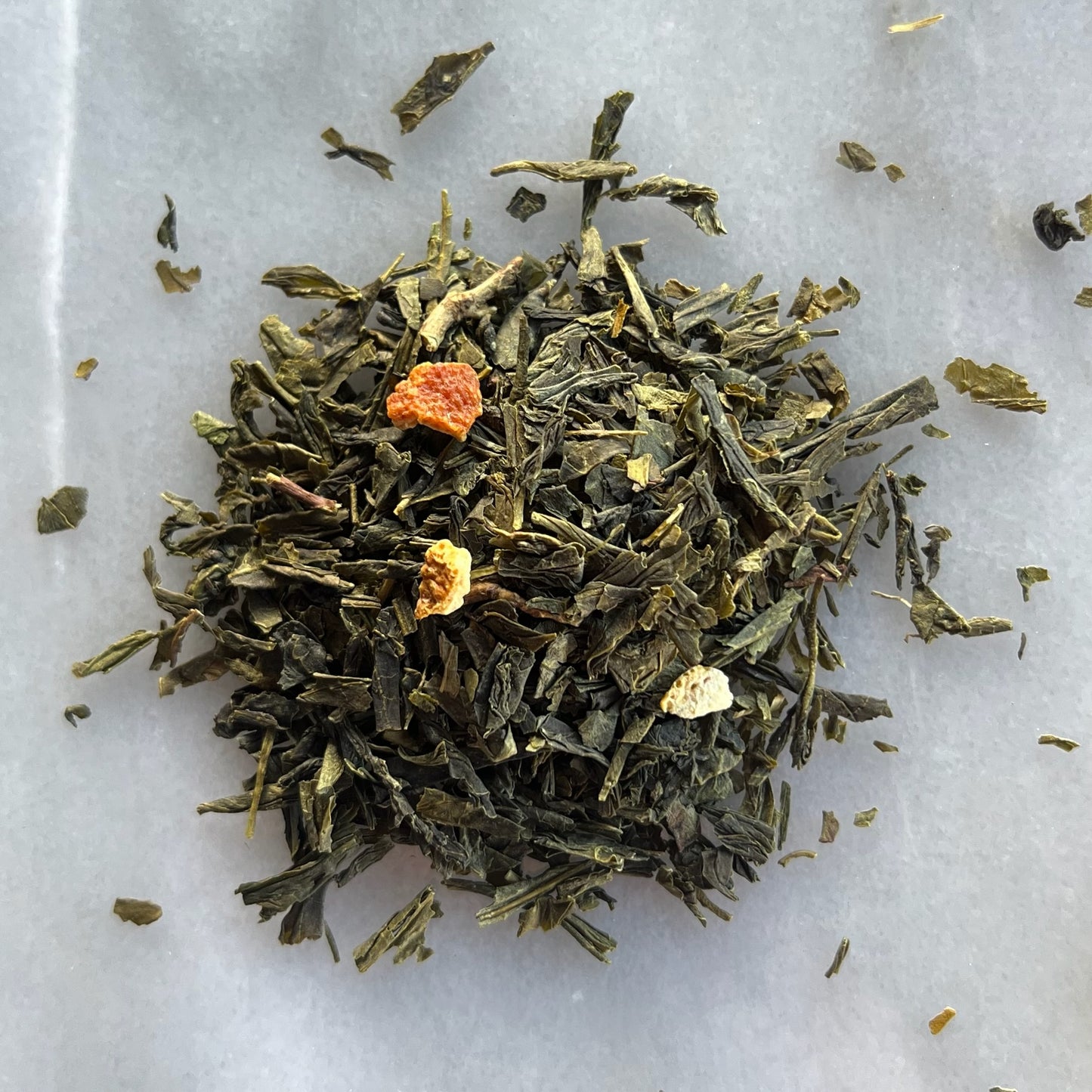 En liten tehög med det gröna teet Sencha Lime, liggandes på en vit marmorbricka där man kan se teets färg och struktur