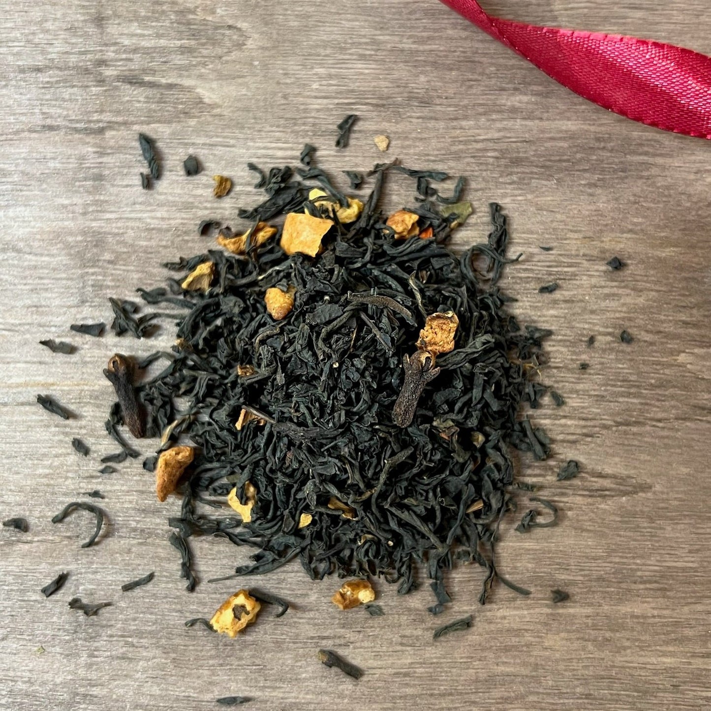 Svart julte vintersaga på en träbricka där man ser teets struktur och innehåll, med ett rött sammetsband i bakgrunden.