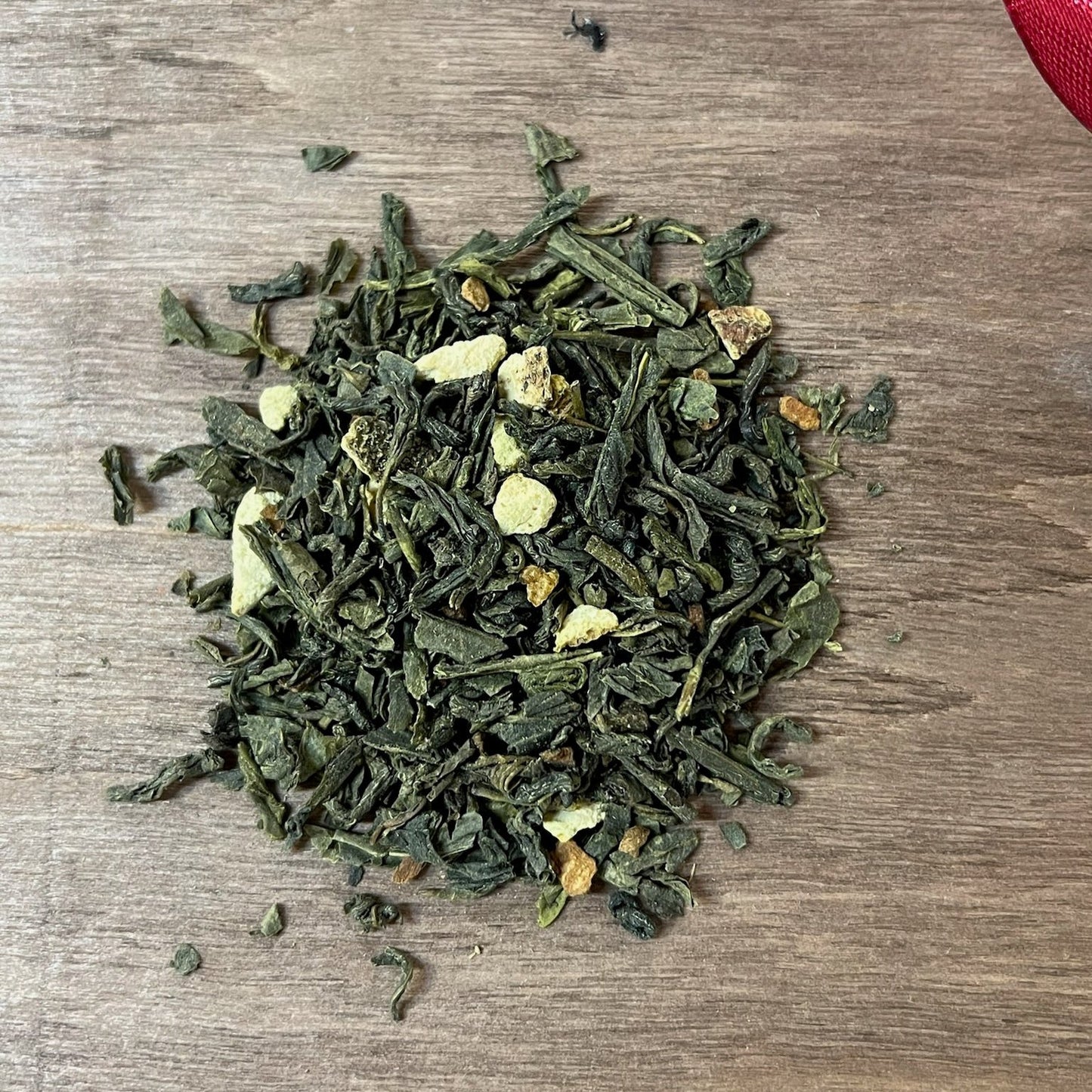 Grönt julte Vintersol på en träbricka där man ser teets struktur och innehåll, med ett rött sammetsband i bakgrunden.
