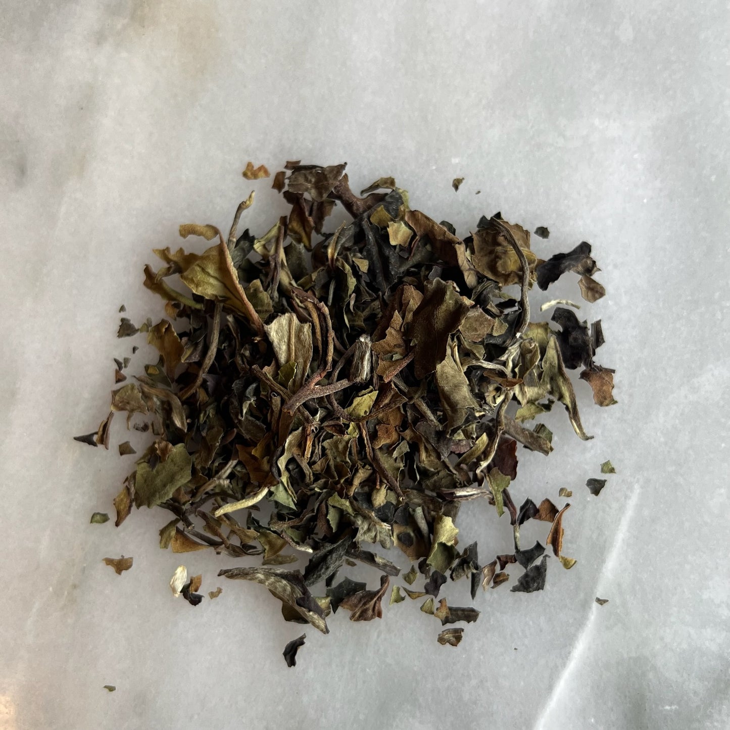 En hög med vitt löste "White Pai Mu Tan" på en marmorbricka som visar teets färg och struktur.