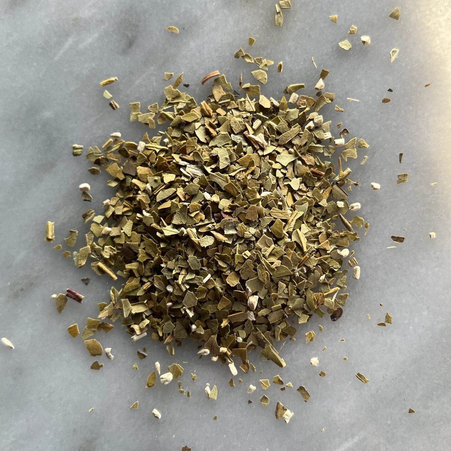 En liten tehög med ört teet Yerba Mate, liggandes på en vit marmorbricka där man kan se teets färg och struktur.