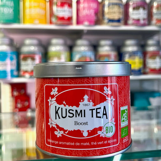 En röd teburk från Kusmi tea med smaken Boost, med flera teburkar i bakgrunden.