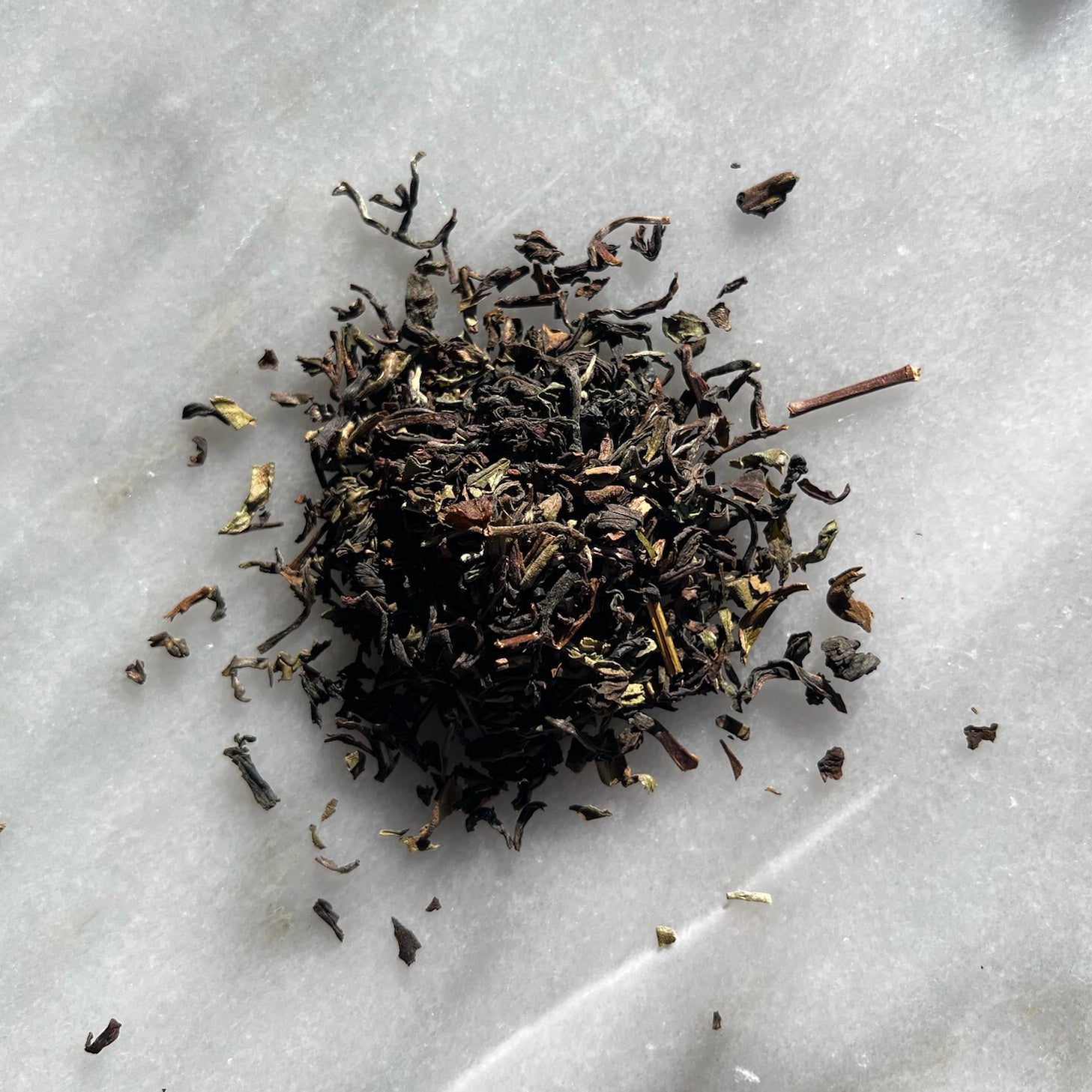 En liten tehög med teet darjeeling first flush, liggandes på en vit marmorbricka där man kan se teets färg och struktur