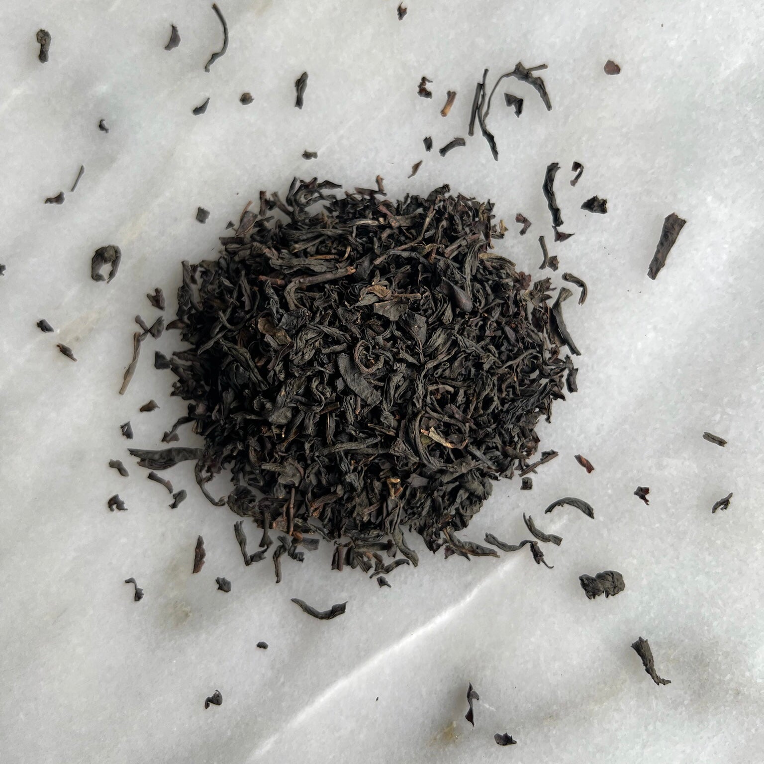 En liten tehög med teet earl grey ekologiskt, liggandes på en vit marmorbricka där man kan se teets färg och struktur